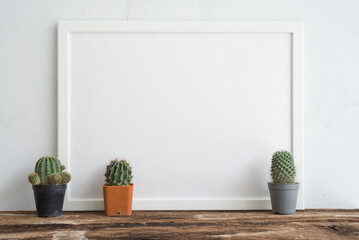 Empty white photo frame and cute cactus pots mockup on wooden table with white wall background copy space. Creative ideas, home decoration design and slow life concept