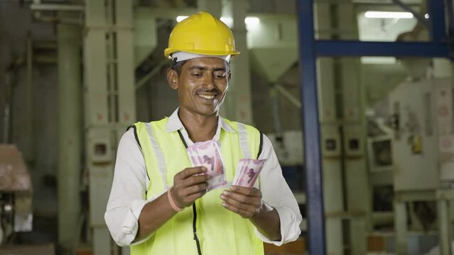 Handheld shot of smiling Industrial worker with hardhat couting money - concept of earnings, banking or financial support and blue collar job