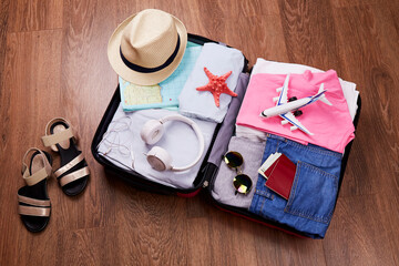 An open suitcase with women's things, a passport and accessories for a vacation. Summer travel, preparation for the trip, packing of luggage. 