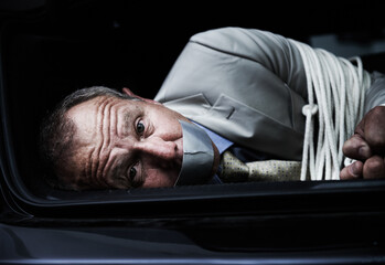 Help me.... Portrait of a frightened businessman lying bound and gagged in the trunk of a car. - obrazy, fototapety, plakaty