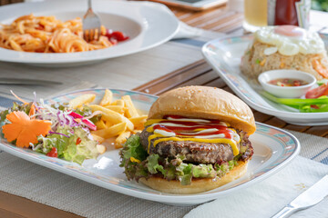A table set on the street in a cafe - a hamburger with a cutlet, French fries and pasta on a sunny summer day on the terrace, a close-up of the outdoor, delicious fast food lunch and breakfast
