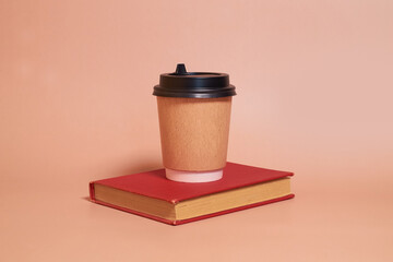 A paper cup with coffee stands on a book on a colored background