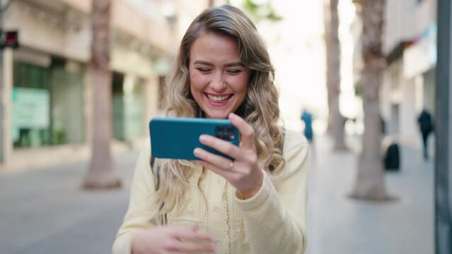 Young blonde woman tourist watching video on smartphone at street