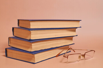 Reading glasses lie next to a stack of books on a colored background. Side view