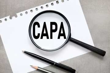 CAPA. abbreviation of corrective action and preventive action. text on magnifier glass on gray...