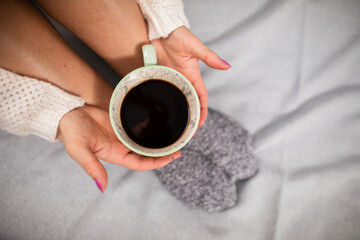 A cup of coffee held in a woman's hands. Neat legs.
