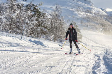 Fototapeta na wymiar Woman with brown hair smiling, wearing ski wear and a backpack skiing down a mountain in ski centre stryn, norway, horizontal
