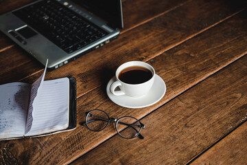 A coffee cup on the desk that has glasses and a notebook computer