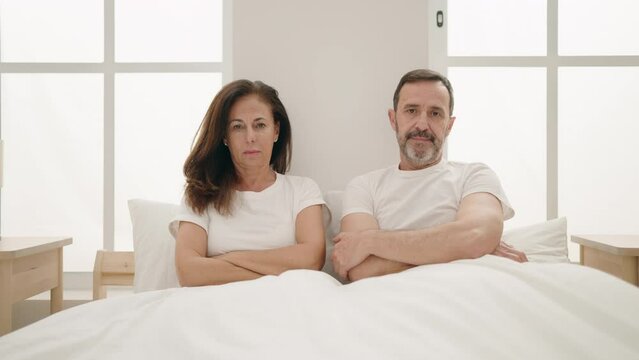 Man and woman couple with serious expression sitting on bed at bedroom