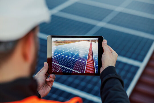 A worker taking a picture of finished solar panels on the roof with tablet.