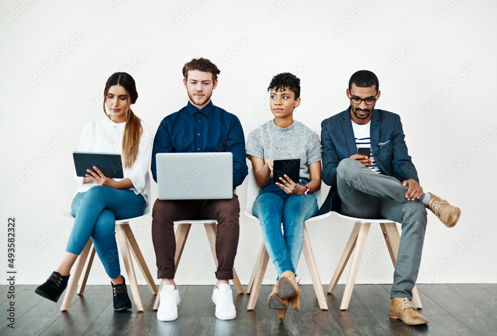 Fototapete Enjoying instant notifications and endless apps. Shot of a group of young people using wireless technology while sitting in a row.