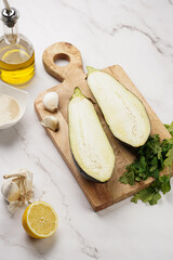 Ingredients for a traditional dish of arabic cuisine baba ganoush: cut in half eggplant, tahin, cilantro, garlic, olive oil, lemon juice on wooden board