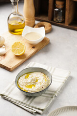 Traditional dish of arabic cuisine baba ganoush made of roasted eggplant, tahin, cilantro, garlic, olive oil, lemon juice on grey background, wooden cutting board, green checkered kitchen towel