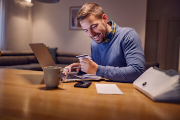 A happy man using credit card for online payment from home.