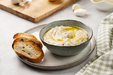 Traditional dish of arabic cuisine baba ganoush made of roasted eggplant, tahin, cilantro, garlic, olive oil, lemon juice with toasted baguette croutons on grey background