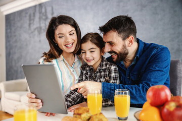 Happy family sitting together at dining table in the morning and using tablet. 