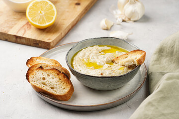 Traditional dish of arabic cuisine baba ganoush made of roasted eggplant, tahin, cilantro, garlic, olive oil, lemon juice with toasted baguette croutons on grey background