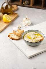 Traditional dish of arabic cuisine baba ganoush made of roasted eggplant, tahin, cilantro, garlic, olive oil, lemon juice with toasted baguette croutons on grey background, white marble board