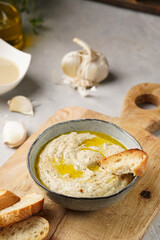 Traditional dish of arabic cuisine baba ganoush made of roasted eggplant, tahin, cilantro, garlic, olive oil, lemon juice with toasted baguette croutons on grey background, wooden board