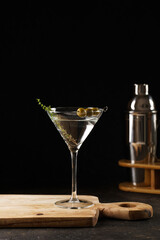 Transparent non-alcoholic beverage with olives and thyme on wooden board on black background and bar equipment