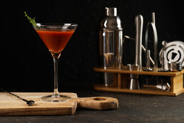 Red non-alcoholic tomato cocktail on wooden board on black background and bar equipment
