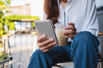 Closeup of a young woman holding and using mobile phone while drinking coffee