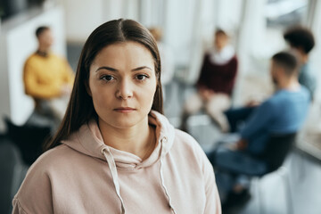 Young woman stands in front of participants of group therapy at mental health center and looks at...