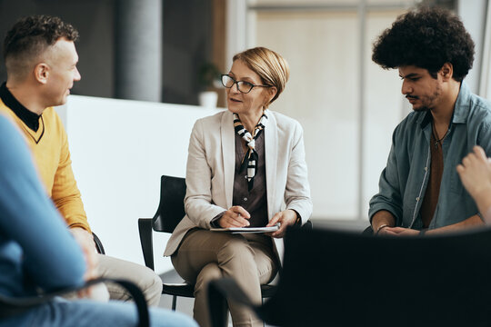 Mature therapist talks to participants of group therapy at mental health center.