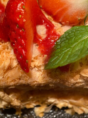 Napoleon cake with a pieces of fresh strawberries close up with selective focus