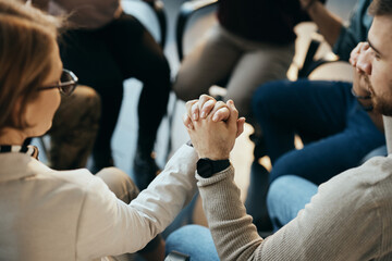 Close up of participants of mental health group therapy holding hands while sitting in circle.