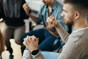 Close up of man holding hands with group therapy members during session at mental health center.