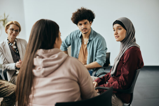Young Muslim woman talks to group therapy members during their meeting at mental health center.