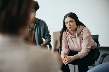 Young woman listens carefully to her therapist during group therapy meeting at  mental health center.