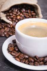 White cup of coffee and roasted fragrant dark coffee grains in bag