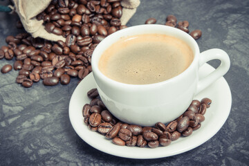 White cup of coffee and roasted fragrant dark coffee grains in bag