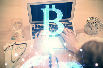 Double exposure of man's hands typing over computer keyboard and crypto currency theme hologram...
