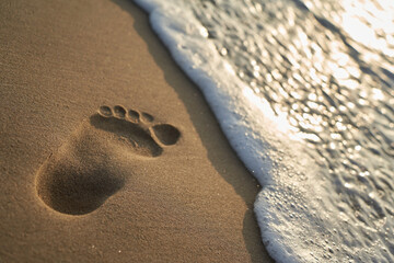 Big footprint from above on the sandy beach. Water edge with foam of the sea. Depth of field.