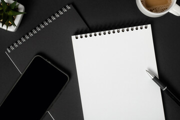 Notebooks with blank white sheets, black pen and mobile phone with black screen, on dark background, copy space, top view. Business or education concept.