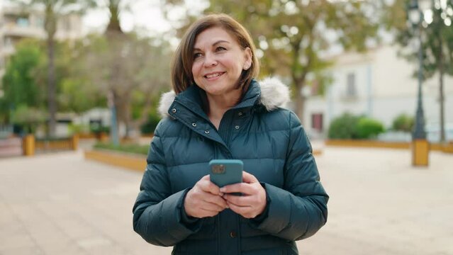 Middle age woman smiling confident using smartphone at park