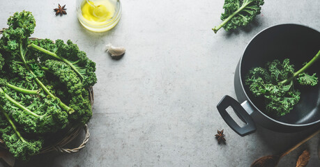 Raw green kale leaves in cooking pot on grey concrete kitchen table with olive oil. Food background...