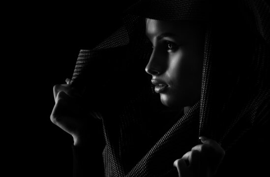 Portrait of a beautiful young girl in a hood on a dark background.Black and white photo.