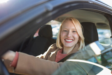 Obraz na płótnie Canvas Young woman sitting in a car. Happy woman driving a car and smiling. Portrait of happy female driver steering car with safety belt. Cute young lady happy driving car.