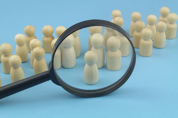 Choosing personnel and hire employers. Wooden figures and magnifying glass on blue background. 