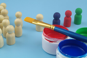 Wooden people figures and different paints with paintbrushes on blue background. Changing people,...