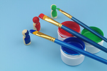 Wooden people figures and different paintbrushes with paint close up. Changing people concept.