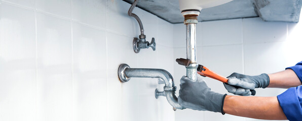 Technician plumber using a wrench to repair a water pipe under the sink. Concept of maintenance,...