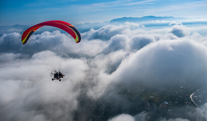 Paramotor is flying in the sky in the morning among white puffy cloud. Evtreme sport concept....