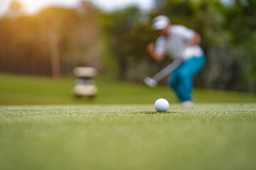Golf balls that are going to be hole by golfers at the green grass golf course at sunset.