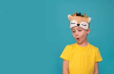 Close-up portrait of a surprised boy, on a blue background. Sleep mask on child's head