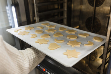 Pastry chef putting cookies of different shapes in oven